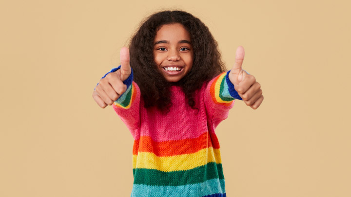Girl with dual heritage wearing rainbow jumper with thumbs up