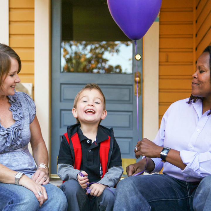 A lesbian couple sitting on steps outside house with boy