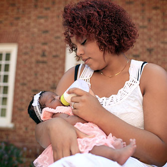 Newborn being bottle fed by mother outside